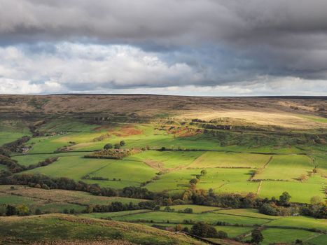 View across the Rosedale valley to the remote Rosedale Ironstone Railway and ruins of the kilns of the East Rosedale Mines picked out by the sunlight, North York Moors National Park, UK
