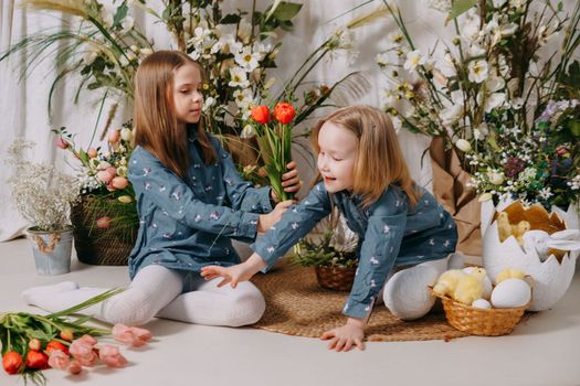 Two girls in a beautiful Easter photo zone with flowers, eggs, chickens and Easter bunnies. Happy Easter holiday