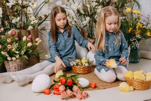 Two girls in a beautiful Easter photo zone with flowers, eggs, chickens and Easter bunnies. Happy Easter holiday