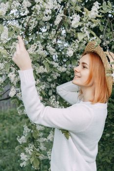 Portrait of a woman in a straw hat in a cherry blossom. Free outdoor recreation, spring blooming garden