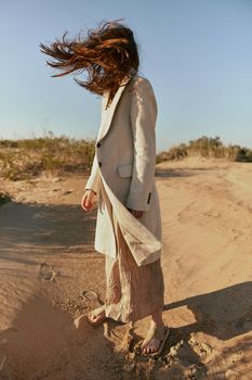 a woman in a light jacket poses on the sand with her face covered by her hair from a strong wind. High quality photo