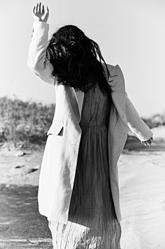 monochrome photo of a woman in a jacket against a clear sky on the coast posing with her hand raised up. High quality photo