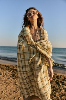 a cute woman stands with a plaid during sunset on the beach and the wind blows her red hair. High quality photo