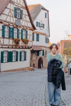 A Beautiful Girl Stands Against The Background Of The Window Of An Old European House. Tourism & Travel Concept. Nice Portrait Of A Young Woman, In Boho Style Outdoors In Fall Autumn Day. Caucasian Female Girl 12 Years Old.