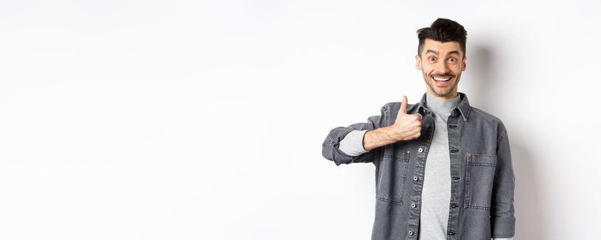 Excited handsome guy showing thumb up and smiling, like good thing, praise awesome choice, looking satisfied and happy, standing on white background.