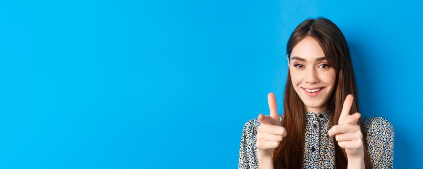 Excited and confident beauty woman, pointing fingers at camera and smiling, invite and beckon you, join us gesture, praising good choice, standing on blue background.