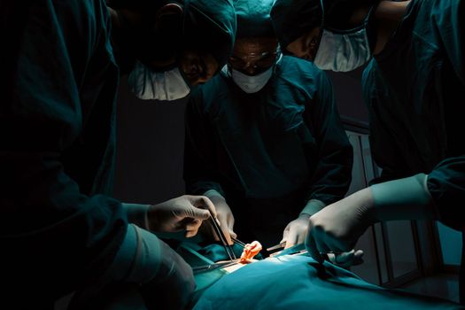 Surgical team performing surgery to patient in sterile operating room. In a surgery room lit by a lamp, a professional and confident surgical team provides medical care to an unconscious patient.