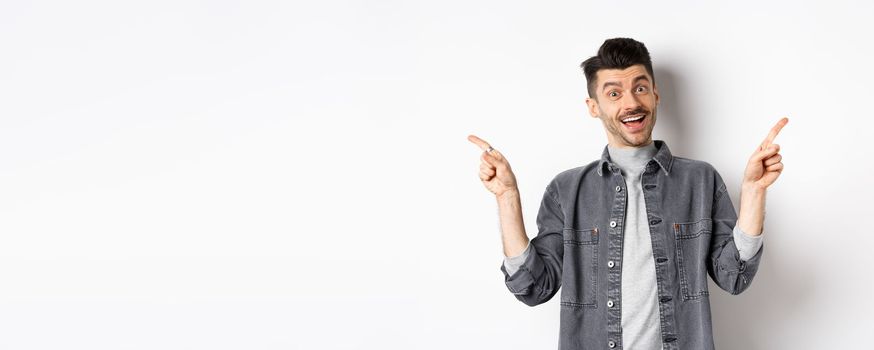 Cheerful smiling man pointing fingers sideways, showing left and right ways, looking happy at camera, standing on white background.