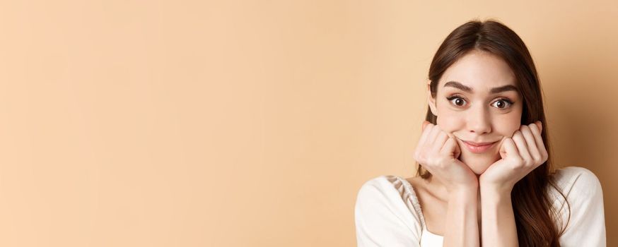 Portrait of intrigued girl listening with interest and excitement, hear interesting story, smiling amused, standing on beige background.