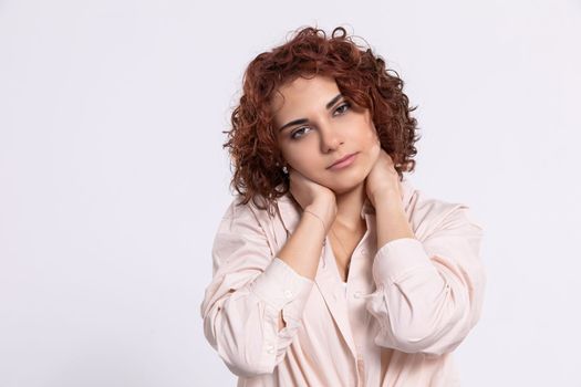 A young girl with short curly chestnut-colored hair. Hand carried up to head height. Light-colored long-sleeved blouse.