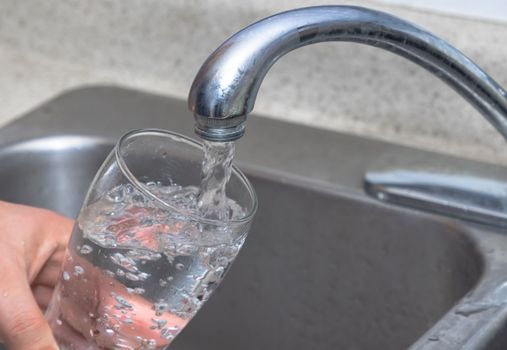 Pouring water into a glass. Filling glass with drinkable water.