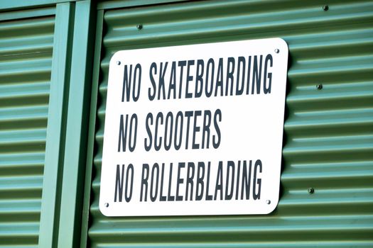 A sign with the text No Skateboarding, No Scooters, No Rollerblading on a metal wall.