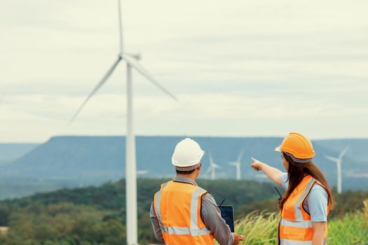 Male and female engineers working on a wind farm atop a hill or mountain in the rural. Progressive ideal for the future production of renewable, sustainable energy.