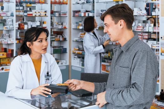 Payment by credit card with payment terminal in qualified drugstore. Modern financial payment of electric money. Caucasian customer purchase medication in pharmacy with prescription from pharmacist.