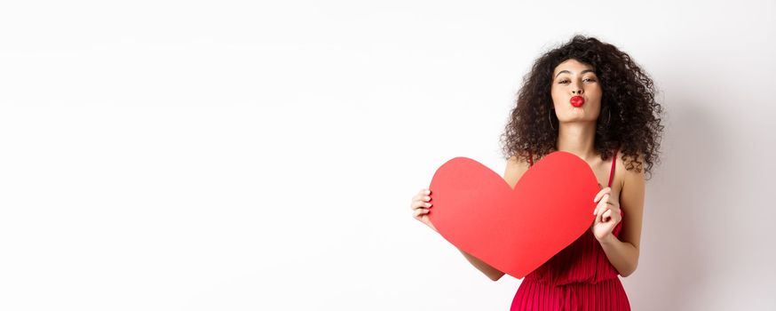 Romantic woman in dress showing big red heart, pucker lips for kiss and express love, express sympathy, white background.