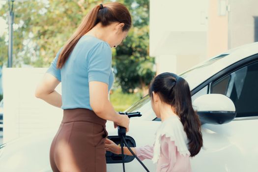 Progressive lifestyle of mother and daughter who have just returned from school in an electric vehicle that is being charged at home. Electric vehicle powered by sustainable clean energy.
