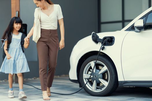 Progressive lifestyle of mother and daughter who have just returned from school in an electric vehicle that is being charged at home. Electric vehicle powered by sustainable clean energy.