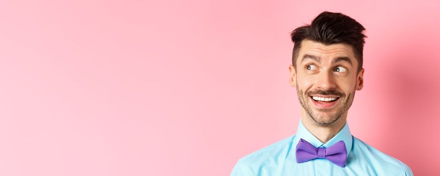 Close-up of amused smiling guy with moustache, pointing and looking left happy, stare at logo, standing on pink background. Copy space