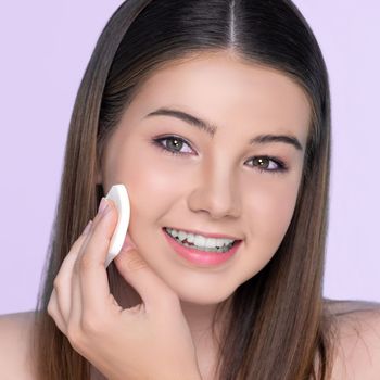 Facial cosmetic makeup concept. Portrait of young charming girl applying dry powder foundation. Beautiful girl smiling with perfect skin putting cosmetic makeup on her face.