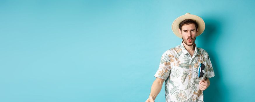 Happy tourist in hawaiian shirt and summer hat dancing, having fun on vacation, standing on blue background.