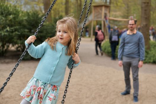 Father rolls daughter on a swing at a park