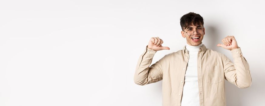 Image of motivated smiling handsome man pointing at himself, self-promoting and clooking confident, standing on white background.