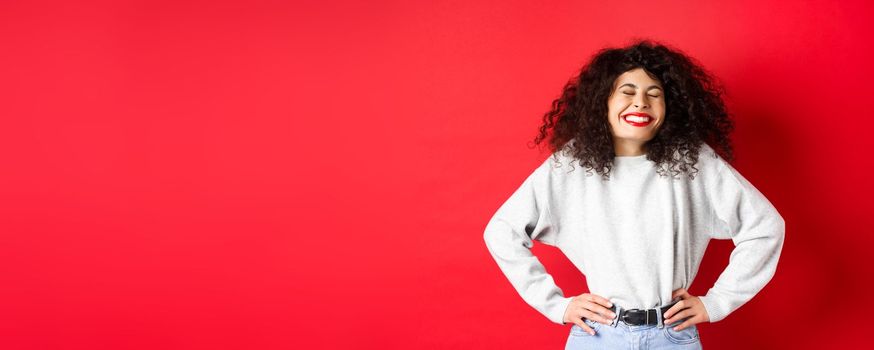 Excited beautiful woman laughing and smiling carefree, enjoying life, standing in sweatshirt against red background.