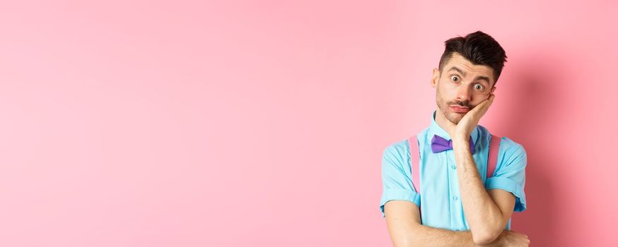 Shocked and tired caucasian guy staring pissed-off at camera, lean on palm and looking at something with skeptical face, standing over pink background.