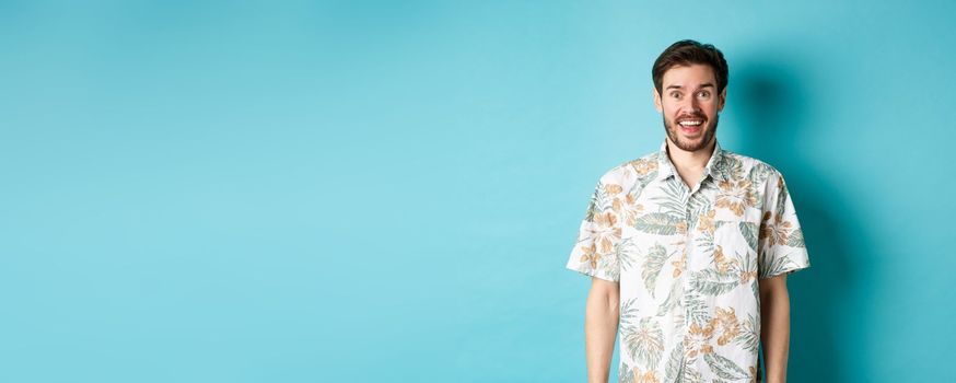 Summer holiday. Handsome happy man in hawaiian shirt looking amused, smiling at camera, standing on blue background.