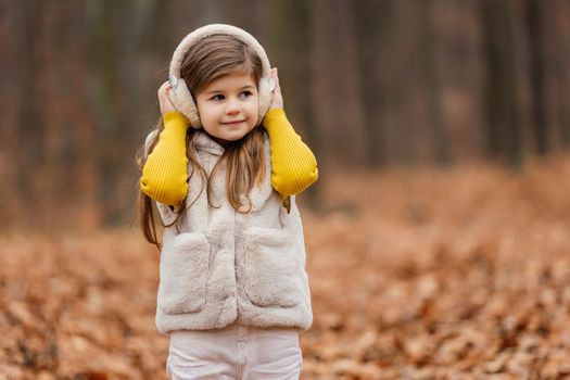 little girl in headphones walks through the autumn forest