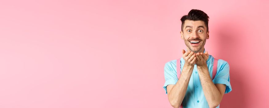 Man in love blowing kiss at camera and smiling passionate, looking at lover happy, enjoying Valentines day, standing over pink background.