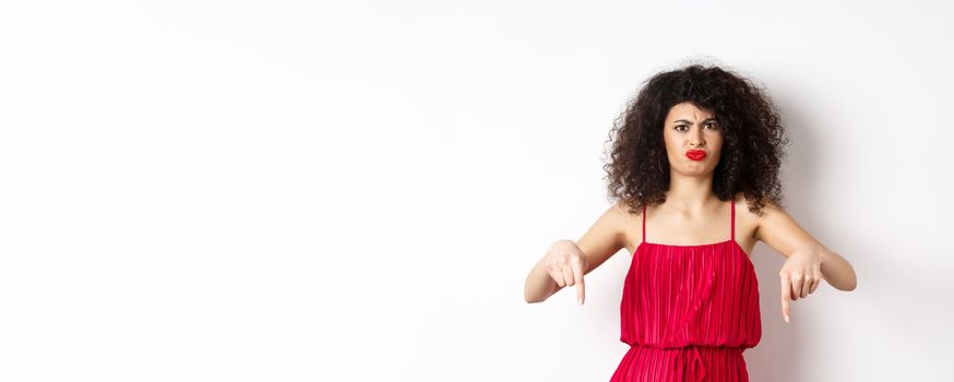 Disappointed caucasian woman in red dress complaining on spoiled date, frowning and grimacing, standing over white background.