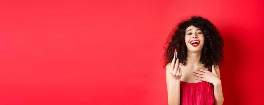 Elegant woman in dress, showing red lipstick and laughing, standing over studio background. Copy space