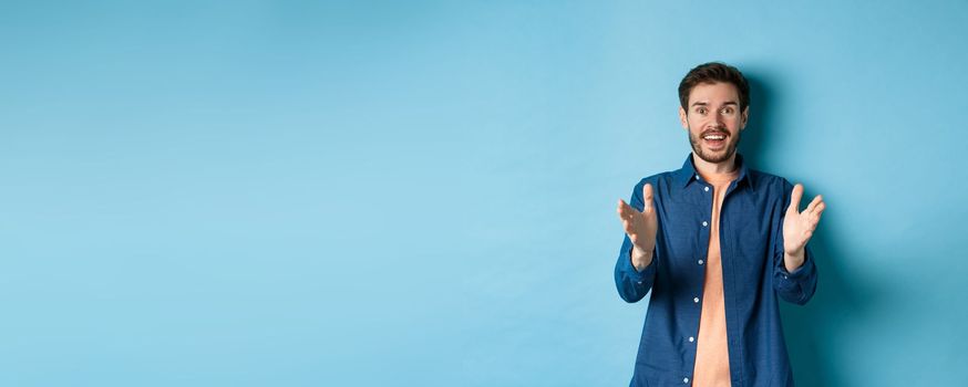 Cheerful young man pointing hands at camera and smiling, feeling glad for you, praising nice work, standing on blue background.