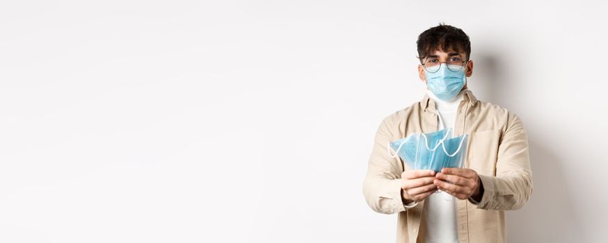 Health, covid and quarantine concept. Image of young guy handing out medical masks for preventive measures, helping during pandemic, standing on white background.