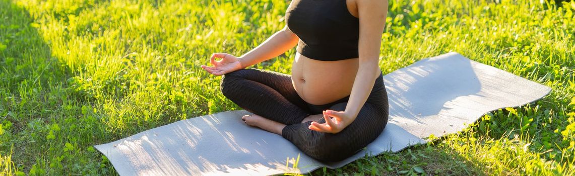 Cute young caucasian pregnant woman is meditating while sitting on a rug on the lawn on a sunny summer evening. Concept of pacification