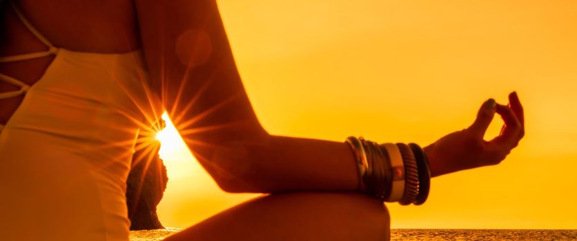 Banner. Young woman practicing yoga on the beach with sunset. Keeps fingers connected, the sun shines through them. The concept of a healthy lifestyle, harmony