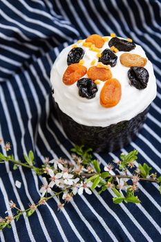 Easter cake, decorated with dried apricots and prunes, stands on a striped blue apron, a flowering branch. Easter religious holiday concept