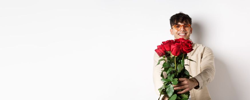 Handsome boyfriend giving you bouquet of roses, make surprise gift on romantic date at valentines day, standing with lover over white background.