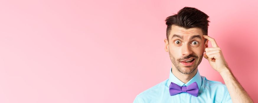 Close-up of confused guy in bow-tie, scratching head and looking puzzled, cant understand something, standing in bow-tie on pink background.