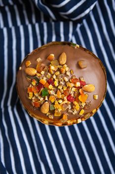 An Easter cake decorated with candied fruits stands on a striped blue apron. Easter religious holiday concept