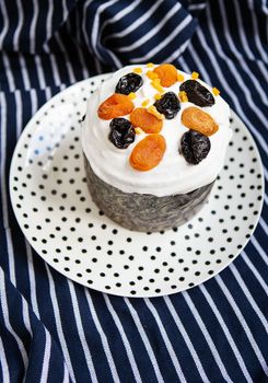 An Easter cake decorated with dried apricots and prunes stands on a plate and a striped blue apron. Easter religious holiday concept