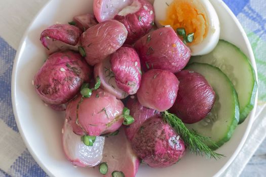 On the table on a plate baked radish with green onions and herbs. Presented in close-up.