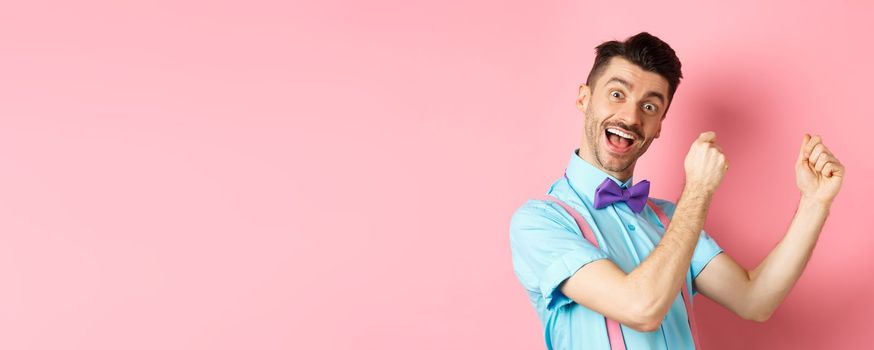 Image of cheerful man celebrating holiday, dancing and having fun, triumphing and saying yes with happy face, standing over pink background.