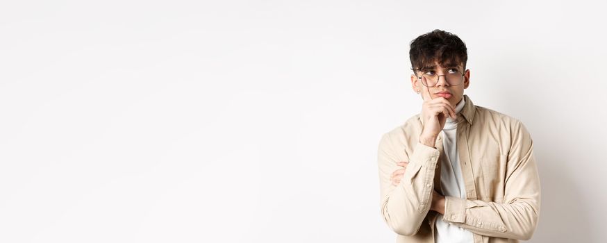Sad and lonely young man looking at empty space with distressed face, standing thoughtful on white background.