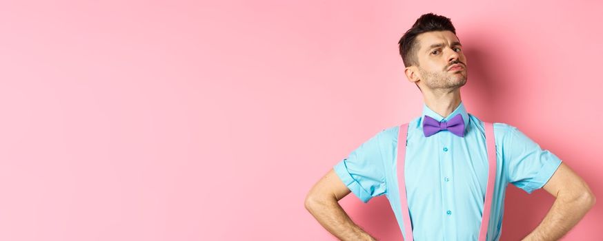 Proud and confident caucasian guy with moustache and bow-tie, looking arrogant with chin up, frowning and looking at camera, standing on pink background.