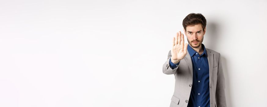 Hold right there. Serious businessman in suit stretch out hand and tell to stop, frowning and look confident, disapprove action, prohibit something bad, standing on white background.