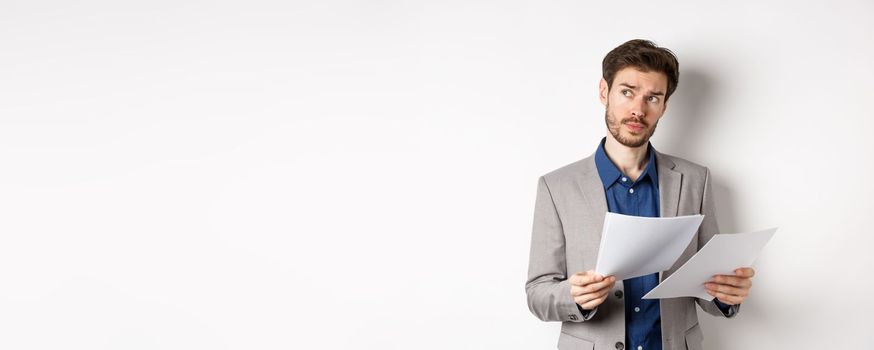 Businessman in suit looking through papers, reading documents at work and thinking, looking aside at logo, standing busy on white background.