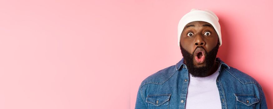 Close-up of impressed Black male model saying wow, staring at camera amazed and wondered, standing over pink background. Copy space