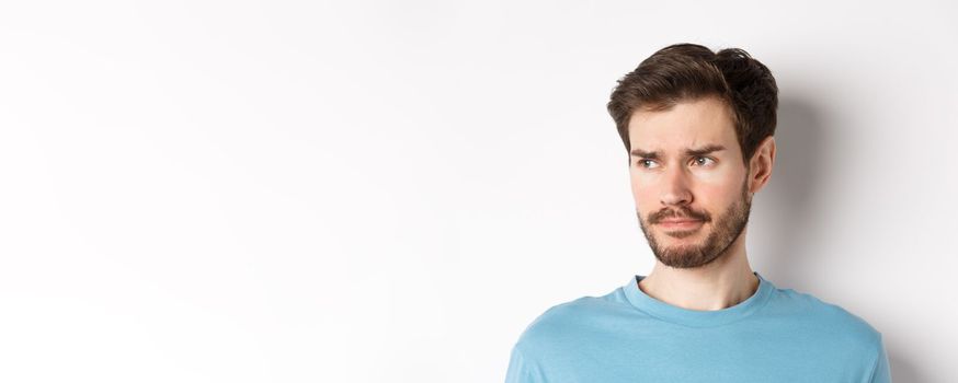 Close-up of disappointed sad man, grimacing and frowning, looking left upset, standing doubtful against white background.